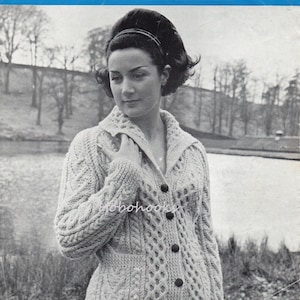May include: A black and white photograph of a woman wearing a light beige knitted cardigan with a honeycomb collar. The cardigan features a cable knit pattern and buttons down the front. The photo is from a vintage knitting pattern.