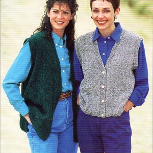 May include: Two women wearing knitted vests. The woman on the left is wearing a green vest and a blue shirt. The woman on the right is wearing a grey vest and a blue shirt. Both women are wearing blue jeans.