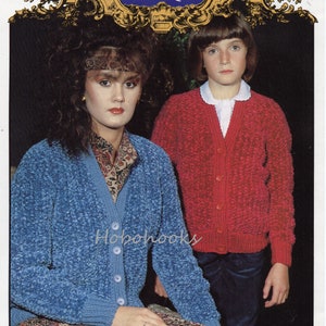 Może przedstawiać: Dwie osoby w dzianinowych kardiganach. Kobieta ma na sobie niebieski kardigan z guzikami, a dziewczynka czerwony kardigan z guzikami. Wzór kardiganu to fakturowany ścieg. Obraz zawiera tekst "Hayfield BAROQUE 1803 26-40"