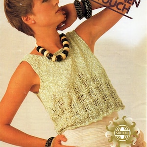 May include: A woman wearing a light green crocheted top with a black and white beaded necklace and black bracelets. The top is a sleeveless design with a delicate lace pattern. The text "THE LINEN TOUCH" is printed in black on a white background.