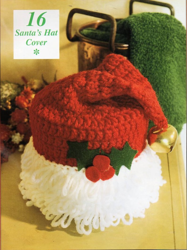 May include: A red crocheted Santa hat with a white yarn beard and a green holly leaf and red berry embellishment. The hat is designed to fit a toilet paper roll. The text "16 Santa's Hat Cover" is printed on a white background.