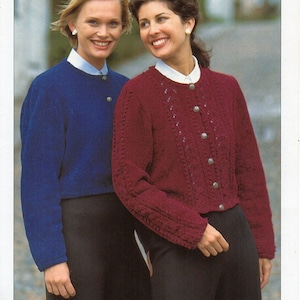 May include: Two women wearing knitted cardigans. The woman on the left is wearing a blue cardigan and the woman on the right is wearing a burgundy cardigan with a cable knit pattern.
