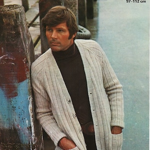 May include: A man wearing a light beige cardigan with a brown turtleneck sweater underneath. The cardigan has a button closure and two pockets. The man is standing next to a wooden post. The image includes the text "PATONS 1397 PRICE CODE B D.K. 38-44 in 97-112 cm".