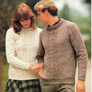Peut inclure: Deux personnes portant des pulls en tricot. La femme porte un pull blanc avec une jupe à carreaux. L'homme porte un pull marron avec un motif en tricot torsadé. Les pulls sont de la marque Patons Capstan.
