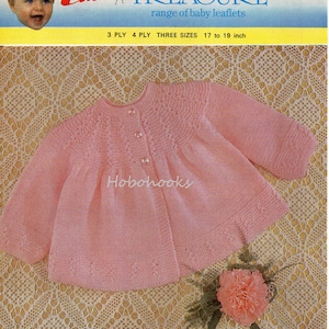 Könnte beinhalten: Ein rosa gestrickter Baby-Cardigan mit Knopfleiste und einem Spitzenmuster. Der Cardigan liegt auf einem weißen Spitzenstoff-Hintergrund. Die Musternummer ist 8545. Emu Treasure Sortiment an Baby-Broschüren. 3-fädig 4-fädig drei Größen 17 bis 19 Zoll.