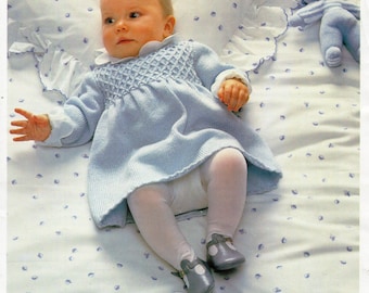 May include: A light blue knitted baby dress with a white collar and a diamond pattern. The dress is 18-22 inches (46-56 cm) and is made with 4 ply yarn. The dress is on a white bed with a blue floral pattern.
