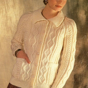 May include: A cream-colored knitted cardigan with a cable knit pattern and a button-up front. The cardigan has two pockets and a collar. The text "Aran" is visible at the top of the image.