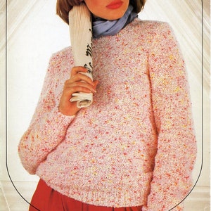 Könnte beinhalten: Ein rosafarbener, weißer und gelber melierter Strickpullover mit Rundhalsausschnitt. Der Pullover wird von einer Person getragen, die eine zusammengerollte Zeitung hält.
