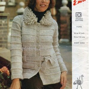 Pode incluir: Um cardigan de malha bege com uma gola branca grande e fofa, um cinto de laço e dois bolsos. O cardigan é mostrado em uma modelo com calças marrons. O número do padrão é 3136 e a lã é DK Double Knitting Fiord. O padrão é para oito tamanhos, de 30 a 44 polegadas ou de 76 a 112 centímetros.