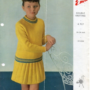 Puede incluir: Un conjunto de punto amarillo de suéter y falda con ribetes azules. El conjunto es para un niño y se muestra en una modelo. El patrón es para punto doble, hilo de 4 cabos, y está disponible en seis tallas para niños de 61 a 86 cm de altura. El patrón es de Emu.