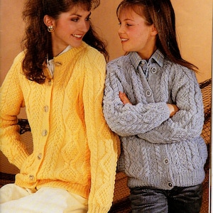 May include: Two women wearing cable knit cardigans. The woman on the left is wearing a yellow cardigan and the woman on the right is wearing a light blue cardigan.