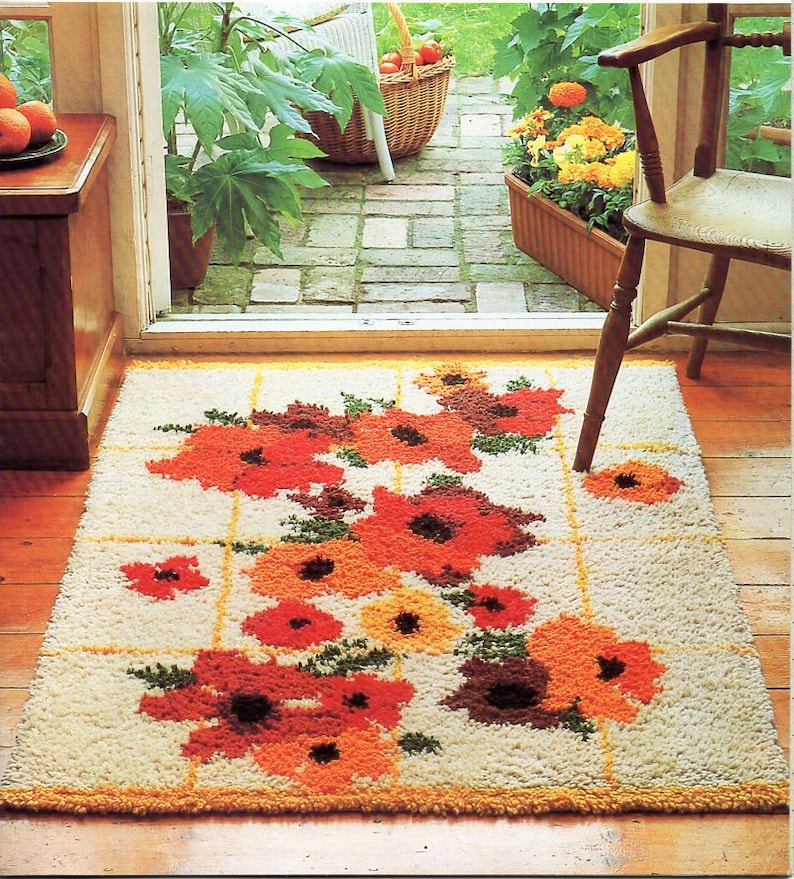 May include: A white rug with a floral design featuring orange, red, and brown flowers. The rug has a grid pattern with yellow lines.