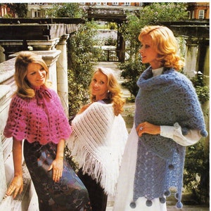 Può includere: Tre donne indossano scialli all'uncinetto. Gli scialli sono rosa, bianchi e blu. Le donne sono in piedi in un giardino. L'immagine è tratta da un libro di modelli di maglia vintage.
