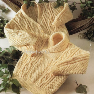 May include: A light yellow knitted cardigan with a V-neck and a matching turtleneck sweater. Both garments feature cable knit detailing on the sleeves and front. The cardigan has three buttons. The sweaters are made of a soft, textured yarn.