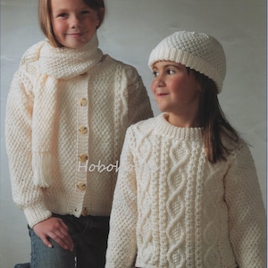 May include: Two girls wearing white knitted sweaters. The girl on the left is wearing a white scarf and has a button-up cardigan. The girl on the right is wearing a white beanie and a cable knit sweater.