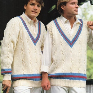 May include: Two white knitted cricket sweaters with blue and red trim. The sweater on the left has long sleeves, while the sweater on the right is sleeveless. Both sweaters have a V-neck and a cable knit pattern.