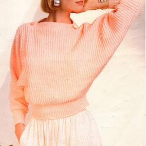 Könnte beinhalten: Ein rosa gestrickter Pullover mit einem Boot Ausschnitt und langen Ärmeln. Der Pullover hat eine gerippte Textur und wird von einem Model mit kurzen blonden Haaren getragen. Der Text "Knit 'n Save Crepe.Dk" ist in der oberen linken Ecke des Bildes sichtbar.