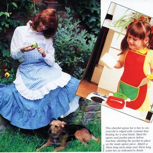 May include: A blue and white gingham apron with a white lace trim and a red and green apron with a yellow trim. Both aprons are for children and have a pocket on the front.