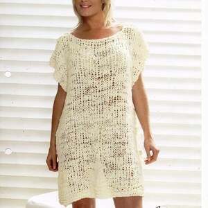 May include: A white crochet dress with a loose fit and a wide neckline. The dress is made with a simple stitch pattern and has a relaxed, casual look. The model is wearing the dress with a natural, effortless style. The image includes the text "Bubble" and "8332 Small - X Large".