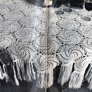 May include: A white crocheted tablecloth with a swirling pattern and fringe. The tablecloth is made of delicate yarn and has a classic, elegant design.