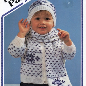 May include: A white knitted cardigan with a purple snowflake pattern, a matching white knitted hat with a purple snowflake pattern, and a white knitted scarf with a purple snowflake pattern. The cardigan has a zipper closure. The hat has a pom-pom on top. The scarf has tassels on the ends. The pattern is for sizes 20-26 inches.