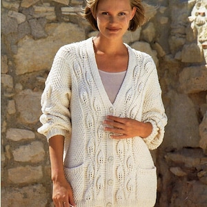 May include: A white knitted cardigan with a cable knit pattern and two pockets. The cardigan has a V-neck and buttons down the front.