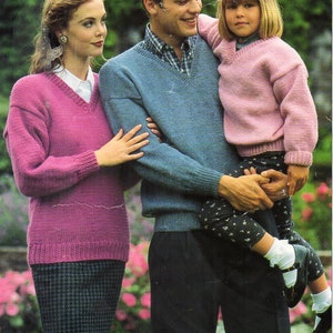 May include: A family wearing matching knit sweaters. The woman is wearing a pink sweater with a black and white checkered skirt. The man is wearing a blue sweater and black pants. The child is wearing a pink sweater and black and white patterned pants.