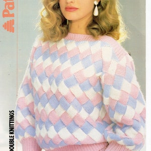 May include: A pink, white, and light blue knitted sweater with a diamond pattern. The sweater has long sleeves and a crew neck. The sweater is made with brushed double knitting.