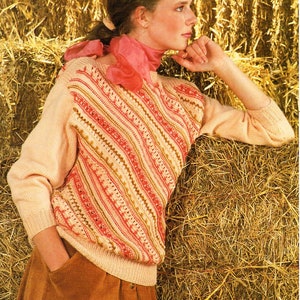 Może przedstawiać: Brzoskwiniowy sweter z ukośnym wzorem w paski w kolorze czerwonym, kremowym i złotym. Sweter ma długie rękawy i okrągły dekolt. Modelka ma na sobie różowy szalik i brązową sztruksową spódnicę.