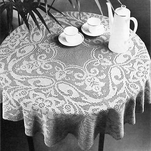 Puede incluir: Un mantel de ganchillo blanco con un delicado patrón floral, con una cafetera y dos tazas y platillos encima.