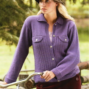 May include: A purple knitted cardigan with a button-up front and two flap pockets. The cardigan has a collar and long sleeves. The model is wearing a brown hat and a red skirt.