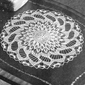 May include: A white crocheted doily with a delicate, intricate design. The doily is circular and features a central motif with radiating patterns.
