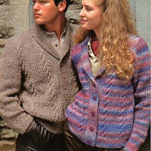 May include: A couple wearing brown and purple knitted cardigans with a cable knit pattern. The woman is wearing a red scarf and the man is wearing a white shirt underneath his cardigan.