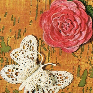 Pode incluir: Uma borboleta branca de crochê com detalhes intrincados e uma rosa rosa de crochê com folhas verdes. Os artigos de crochê são exibidos em um fundo marrom texturizado.