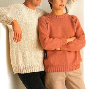 May include: Two people wearing knitted sweaters. One sweater is a light beige color, and the other is a reddish-orange. The sweaters have a ribbed hem and cuffs. The person on the left is wearing black pants, and the person on the right is wearing tan pants.