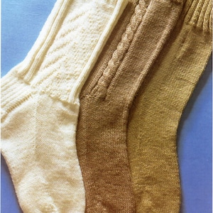 May include: Three pairs of hand-knitted socks in different colors and patterns. The socks are made with a cable stitch and a textured stitch. The socks are a light cream color, a light brown color, and a darker brown color.