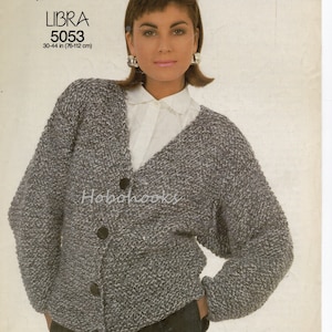 Peut inclure: Un cardigan en tricot épais gris et blanc avec un col en V et une fermeture à boutons. Le cardigan est présenté sur un mannequin et mesure 76 à 112 cm.