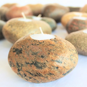 May include: A collection of brown and gray stone candle holders with white tea lights. The candle holders are shaped like smooth, rounded river rocks.