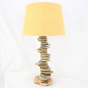 May include: A table lamp with a beige lampshade and a base made of stacked stones.