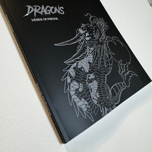 May include: A black book with a silver dragon illustration on the cover. The title "DRAGONS" is printed in silver lettering above the author's name, "DEREK DUFRESNE", which is also printed in silver lettering.