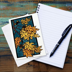 May include: A card with a stylized illustration of a branch of oak leaves in shades of yellow and orange against a teal background. The leaves are outlined in black and the acorns are brown.