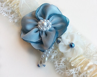May include: A white lace garter with a blue flower and pearl embellishments.