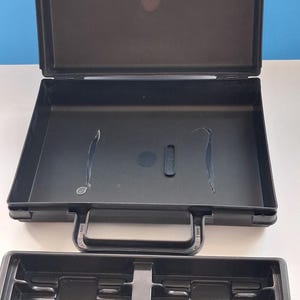 May include: Black plastic carrying case with an open lid and a separate tray. The case has a handle and a latch. The tray has multiple compartments. The background is white and blue.