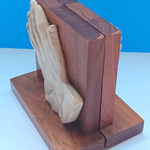 May include: A pair of wooden bookends with a hand sculpture. The bookends are made of dark brown wood and have a rectangular base. A beige hand sculpture is attached to one of the bookends, adding a unique decorative element.