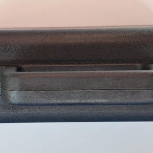 May include: A black, rectangular carrying case with a handle and two latches. The case is made of a textured material and appears to be closed. The handle is centered on the top of the case.