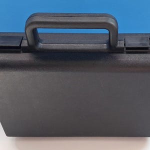 May include: A black, rectangular carrying case with a handle and two latches. The case is made of a textured material and sits on a white surface with a blue background.