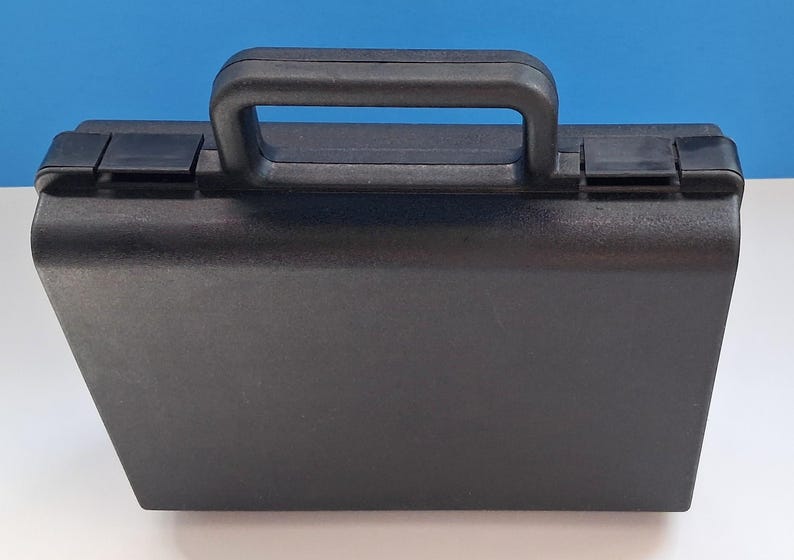 May include: A black, rectangular carrying case with a handle and two latches. The case is made of a textured material and sits on a white surface with a blue background.