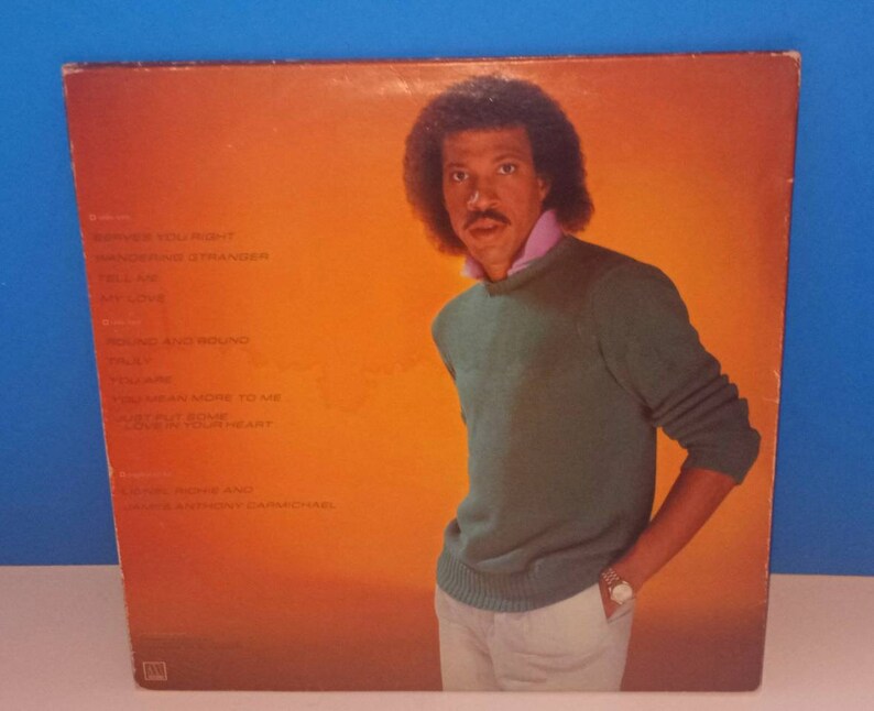 May include: Album cover featuring a portrait of Lionel Richie in a green sweater and pink collared shirt against an orange background. The album's tracklist is visible on the left side. The album is vintage.