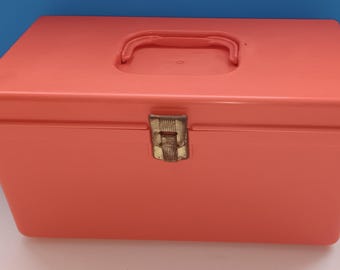 Puede incluir: Una caja de almacenamiento de plástico naranja brillante con un cierre dorado y un asa en la parte superior.