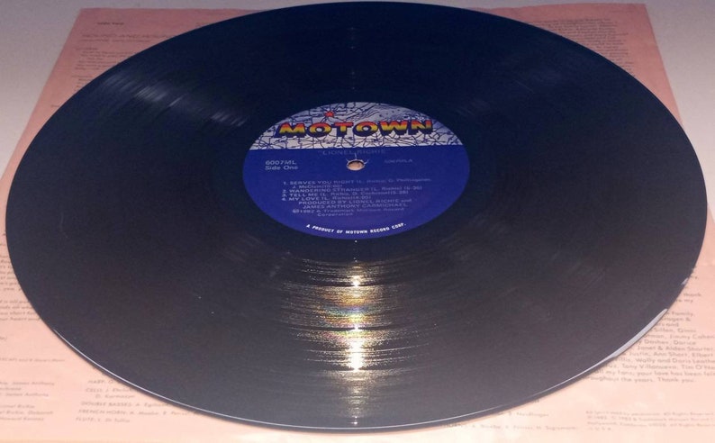 May include: A black vinyl record with a blue and white label featuring the Motown logo. The record is on a light pink background with text. The label lists song titles and artist names. The record is a vintage music item.